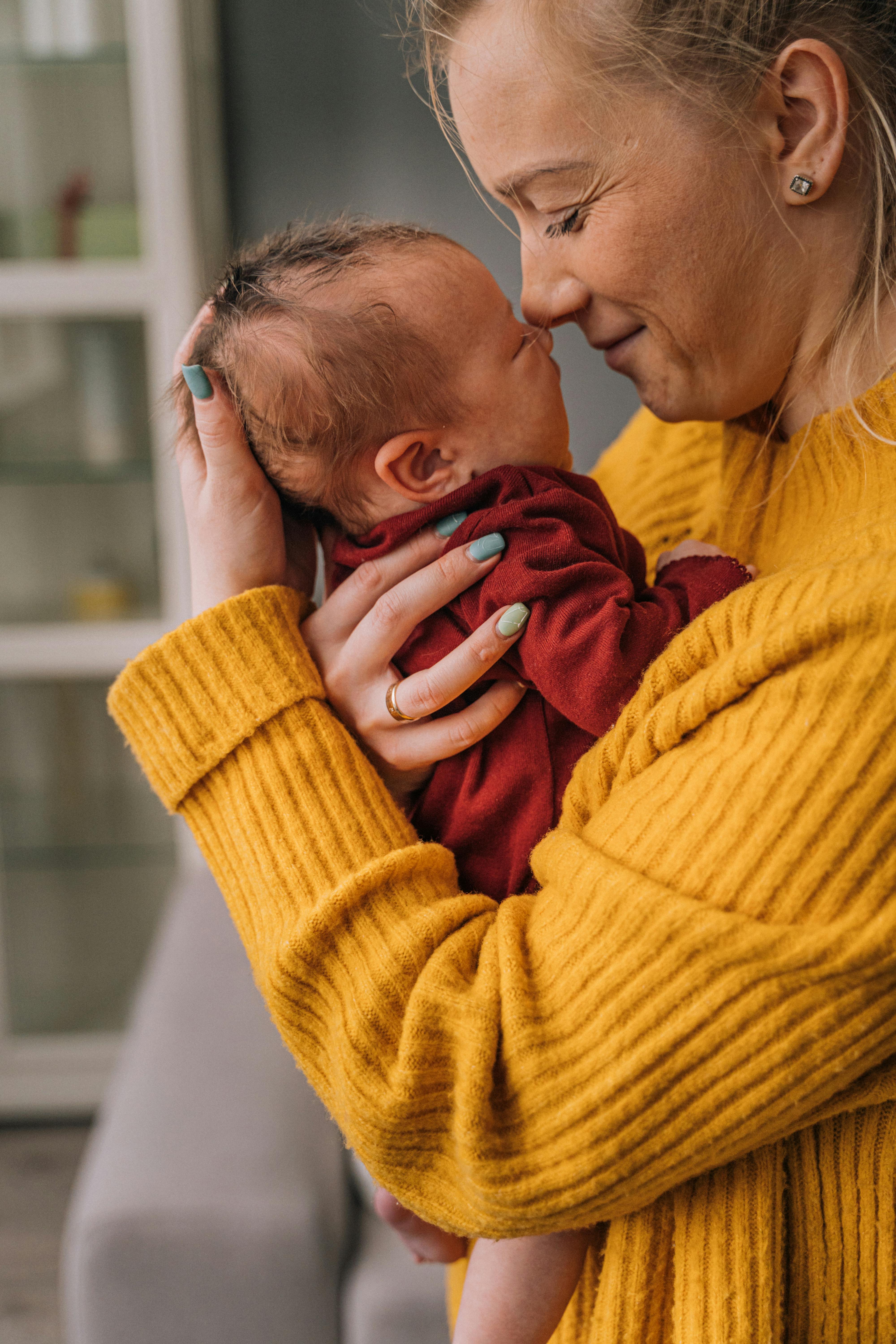 A mother in a yellow sweater holding her baby close